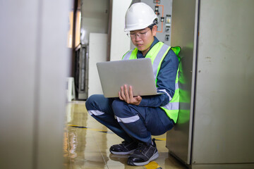 Engineer in power station control room wearing safety helmet and reflective vest working on laptop...
