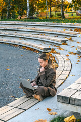 Young woman working remotely by a lake on a laptop. Digital nomad lifestyle, freedom, nature,...