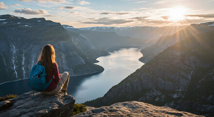 Adventurous woman hiker enjoys scenic sunset view from mountaintop overlooking a breathtaking fjord landscape, feeling peaceful and serene.