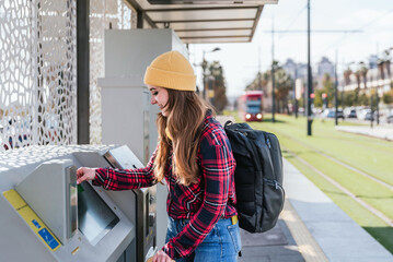 Young female student paying for public transport at station ticket machine