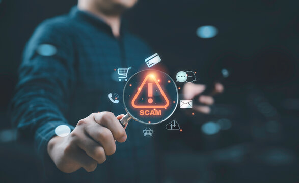 Businessman holding magnifier glass inside with glowing red exclamation waring caution sign with technology including credit card calling e-mail message cloud computing for alert cybersecurity concept