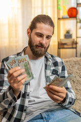 Young man checks fresh earnings salary at home, slowly counting each money dollar cash banknotes...