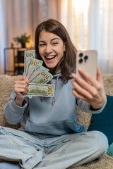 Smiling young woman blogger influencer recording story on smartphone sitting on sofa couch showing...