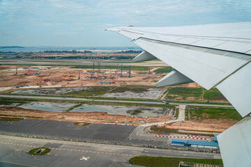 Aerial shot showcases airplane wing against a land in progress. Construction work, machinery, and...