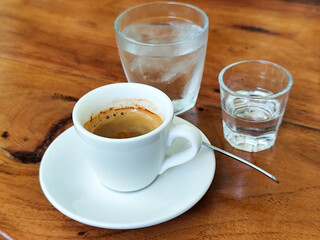 A cup of hot espresso served with a glass of liquid sugar, and a large glass of ice water on a...
