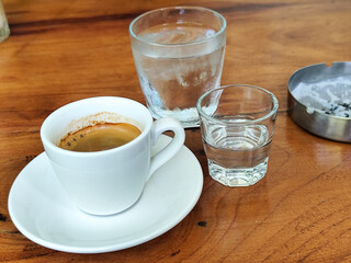A cup of hot espresso served with a glass of liquid sugar, and a large glass of ice water on a...