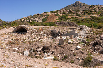 Ancient ruins in Turkiye, featuring stone structures and an archway. The landscape includes rocky...
