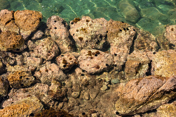 Clear turquoise water over rocky shoreline in Turkiye. Sunlight reflects off the water, revealing underwater rocks and marine life.