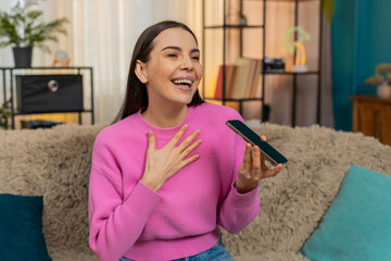 Young woman at home talking on smartphone using speaker mode, emotionally sharing story with...