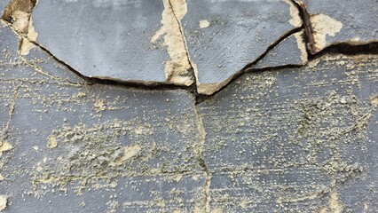 The old dark grey cement wall is broken, the paint is peeling, damaged, and has stains. The old...