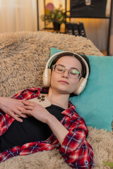 Young woman wears wireless headphones on home sofa, nodding as she listens to audiobook with deep...