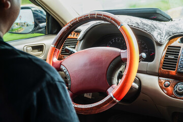 A person driving, showcasing the interior of a car with focus on the steering wheel. The wood grain...