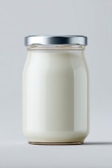 Clear glass jar with silver lid filled with creamy white yogurt on a plain light background perfect for dairy product packaging and health food themes