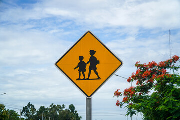 A bright yellow school crossing sign stands against a partly cloudy sky, cautioning drivers....