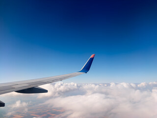 Airplane wing over cloudy landscape under clear blue sky at high altitude