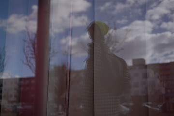 A person is standing thoughtfully in front of a large window, observing a beautiful reflection of a cloudy sky overhead, which adds to the atmosphere