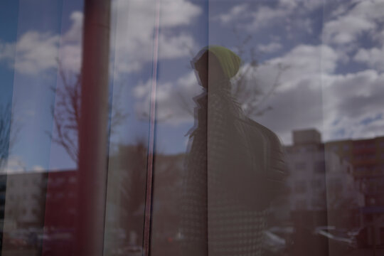 A person is standing thoughtfully in front of a large window, observing a beautiful reflection of a cloudy sky overhead, which adds to the atmosphere