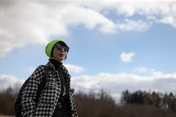 A woman who is wearing a stylish green hat along with trendy sunglasses is standing in front of a...