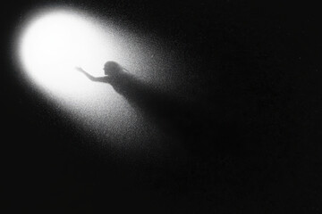Silhouette of a person reaching towards a bright light in a dark and grainy environment image