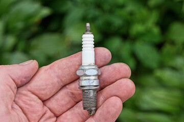 one small metal white gray spark plug lies on the open palm of the hand on a green background on a summer street