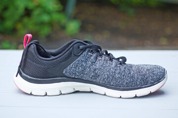one gray black sneaker made of fabric and leather with white sole stands on a wooden table on a...