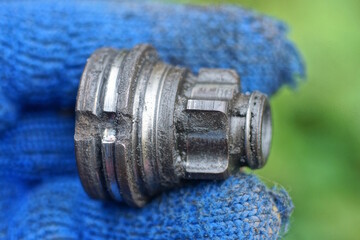 hand in blue glove holds black gray old iron part from bicycle hub on summer street on green...