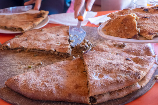 Medfouna, Berber pizza cut into slices, traditional and rustic culinary dish originally from the Morocco. Taken in Rissani Sahara desert, blurred background
