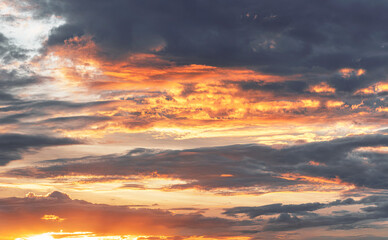 Dramatic evening sky with glowing orange clouds illuminated by the setting sun against a dark and moody background.