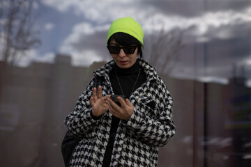 A woman sporting a bright neon yellow hat along with stylish sunglasses is intently looking at her...