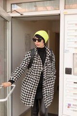 A stylish woman dressed in a bright yellow hat and trendy sunglasses is confidently standing in a...