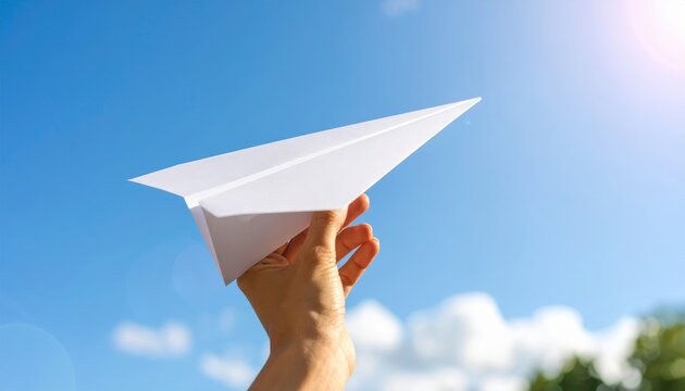 Hand Holding Paper Airplane Against Bright Clear Blue Sky