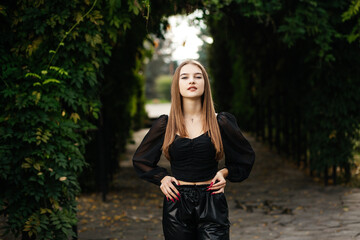 Girl on a summer day near a green tunnel in black leather pants