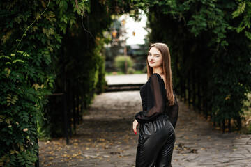 Girl on a summer day near a green tunnel in black leather pants