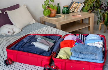 Open suitcase overflowing with clothes on bed in bedroom for a trip. Take with you the necessary pills and medicines, cosmetic accessories, beauty products and clothing. Getting ready for a vacation.