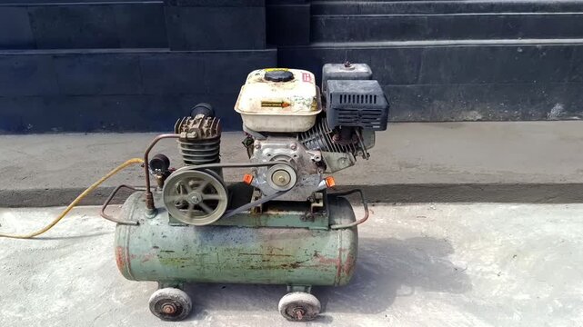 Video footage of an old, rusty portable air compressor powered by a gasoline engine, with small wheels on the bottom of the tank for mobility.