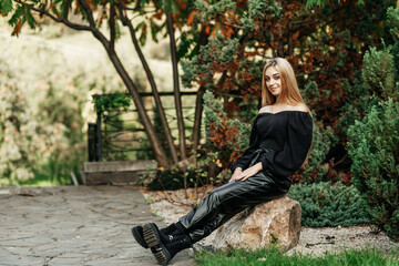 A girl sits on a rock on a summer day, she is wearing leather pants