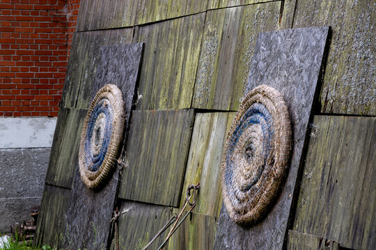 Two weathered straw archery targets mounted on a moss-covered wooden wall. The rustic setting highlights the charm of traditional archery practice in an outdoor environment.