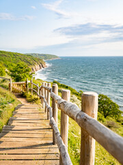 Obraz premium Holztreppe am Wanderweg um den Hammerknuden, Blick auf die Küste, leicht bewölkter blauer Himmel, vertikal