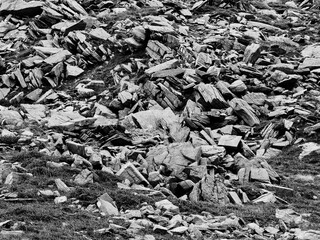 A monochrome mountain landscape displays a field of sharp, angular rocks and sparse grass. Stones of various sizes are scattered across the slope.