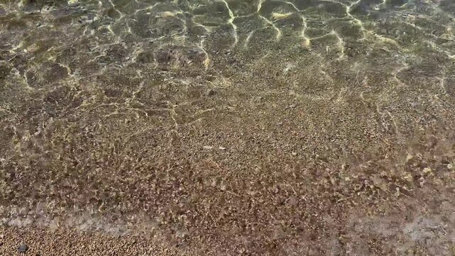 Clear water gently lapping against sandy beach, creating beautiful natural patterns and textures