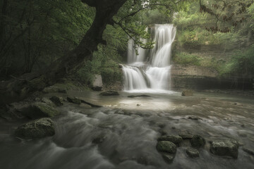 Scenic waterfall in Peñaladros, Burgos, Spain. Lush green forest landscape with mossy rocks and...