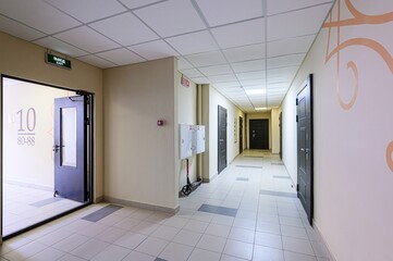 well-lit hallway with tiled floors, multiple apartment doors, exit signs, and neutral-colored walls with light orange swirls