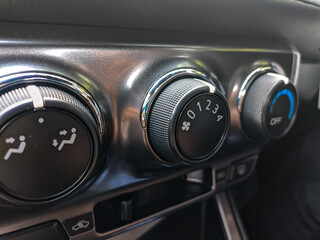 Close-up of the AC control panel with three setting knobs (airflow direction, fan speed, and cooling temperature). Interior view of a modern vehicle with basic climate control.