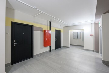 interior shot of an apartment hallway featuring black doors, a red fire cabinet, gray tile flooring, and neutral-toned walls with color accents