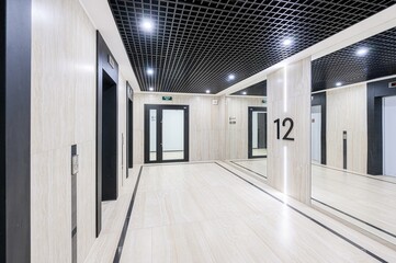 Modern interior with elevators, doors, and reflective surfaces. The ceiling is black grid, and the...