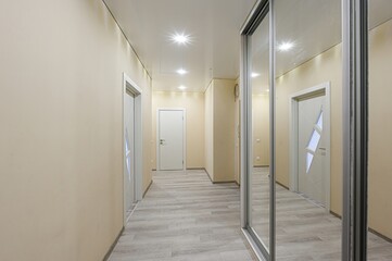 well-lit hallway with beige walls, light wood flooring, white doors, and a large sliding mirrored wardrobe
