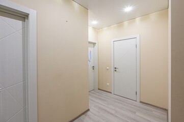 bright hallway with beige walls, white doors, light wood floors, and recessed lighting. Clean, modern design