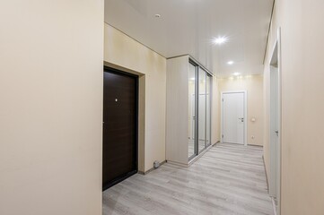 well-lit hallway with light beige walls and a glossy white ceiling. Features include a dark wooden...