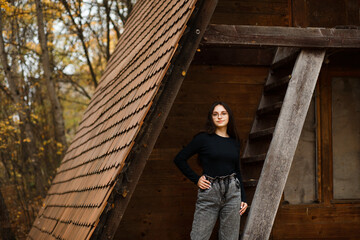 Girl in jeans and a black sweater in the forest in autumn near an old house