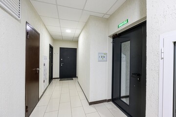 bright hallway features white textured walls, tiled floors, and several doors. An exit door with a...